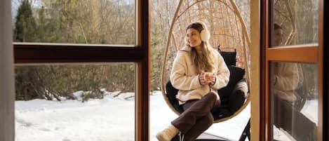 A person sitting in a hanging chair by a window with a snowy landscape view.