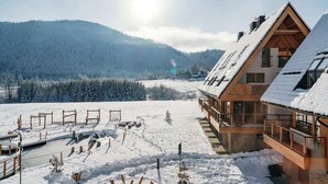 A wooden chalet with a sloped roof, a balcony, and a view of a snowy mountain landscape.