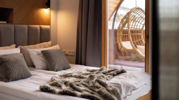 A bedroom with a bed, a fluffy blanket, a hanging chair, and a view of the outdoors.