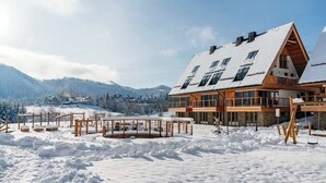 A large wooden chalet with multiple balconies, surrounded by snow-covered terrain and mountains.