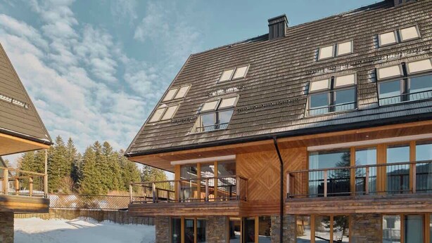 Ein modernes, zweistöckiges Gebäude mit großen Fenstern, einem Balkon und einer steinernen Fassade.