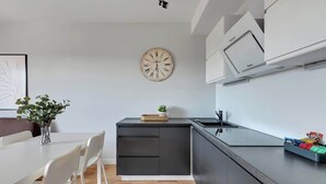 Una cocina moderna con un reloj de madera, una mesa de comedor con sillas y una pequeña planta en la encimera.