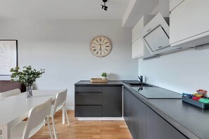 Eine moderne Küche mit einer Holz-Uhr, einem Esstisch mit Stühlen und einer kleinen Pflanze auf der Arbeitsfläche.
