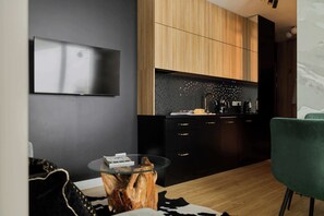 Ett modernt kök med en platt-TV, träskåp, en svart bänkskiva och en grön stol.