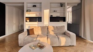 Ein modernes Wohnzimmer mit einem beigen Sofa, einem runden Couchtisch und integrierten Regalen mit dekorativen Accessoires.