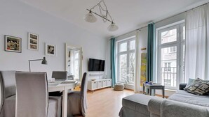 Una sala de estar moderna con un sofá, una mesa de comedor, un televisor y una ventana con cortinas.