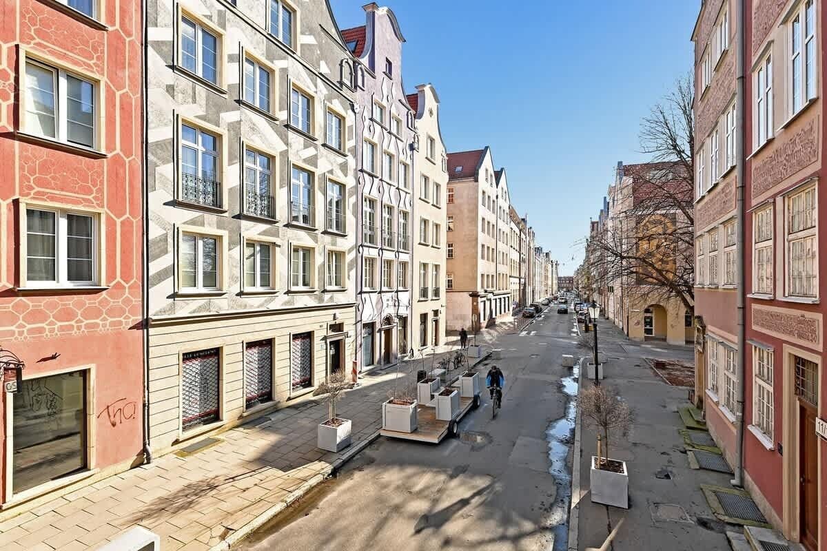 Una calle bordeada de edificios de varios pisos, algunos con balcones, y un ciclista en la vía.