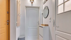 Un pasillo con una puerta de madera, una puerta blanca, un taburete pequeño, un espejo y un armario.