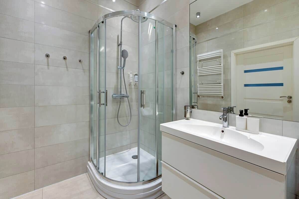 Ein modernes Badezimmer mit einer Glastrennwand zur Dusche, einem weißen Waschtisch mit Spiegel und einem gefliesten Boden.