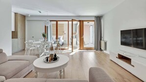 Una sala de estar moderna con un sofá, una mesa redonda de centro, un televisor y un comedor con sillas y una mesa.