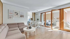 Una sala de estar moderna con un sofá, una mesa redonda para café y un comedor con sillas. Hay una puerta corrediza de vidrio que da a un balcón con una cama.