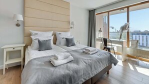 Habitación de hotel moderna con una cama grande, mesitas de noche, una silla y vistas de la ciudad a través de grandes ventanales.
