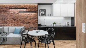 Une cuisine moderne avec un mur d’accent en briques, un coin repas avec une table ronde et des chaises, et un canapé gris agrémenté d’un plaid.