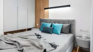 Une chambre moderne avec un lit gris, des coussins bleus, un mur d’accent en bois et une table de chevet sur laquelle se trouve une tasse.