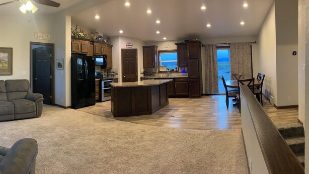A spacious living area with a kitchen, dining area, and a view through a door. - Spacious 4-bedroom house in charming rural Powell with media and fitness room (Powell)