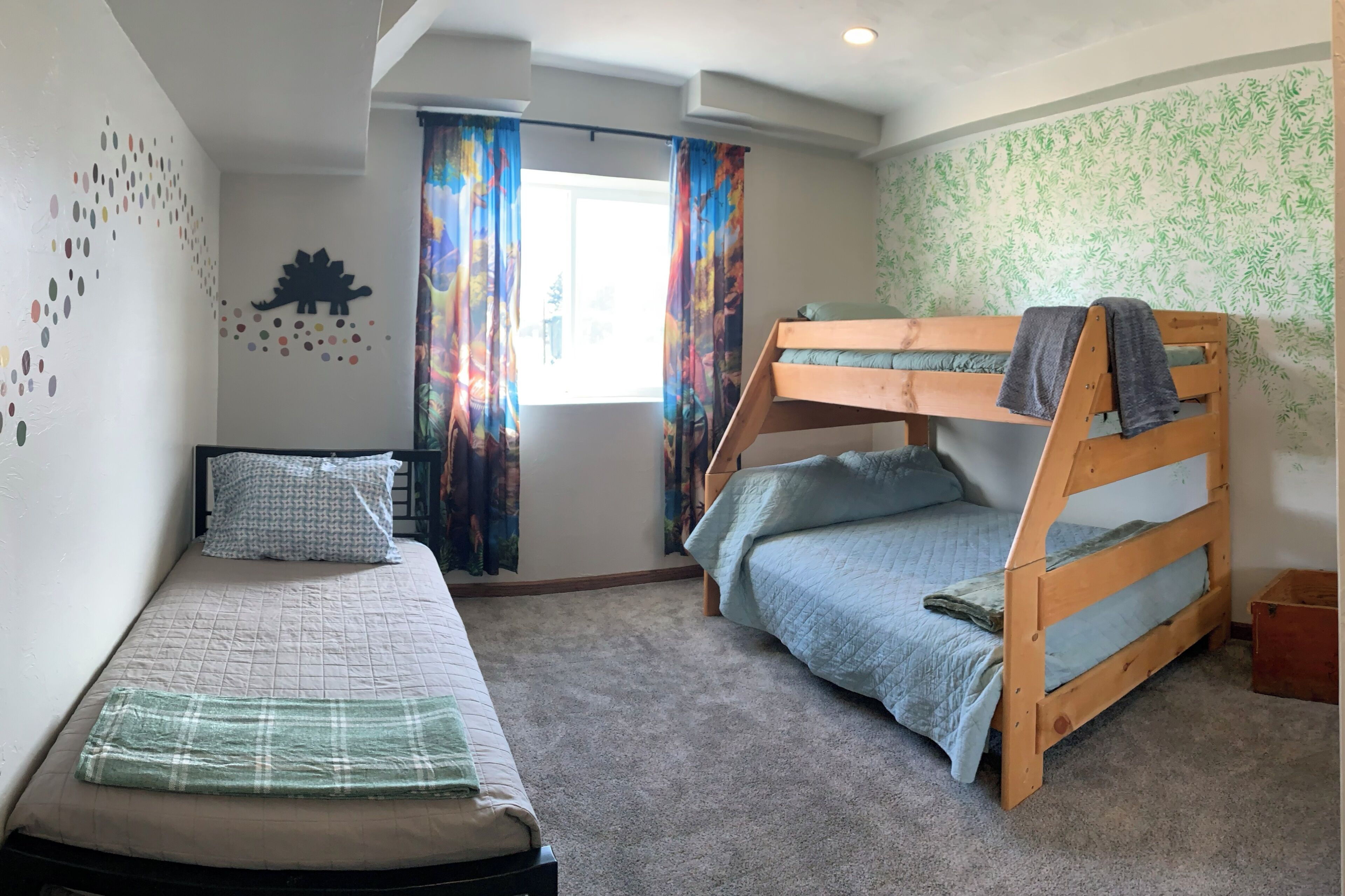 A bedroom with a bunk bed, a single bed, a window with curtains, and a wall decal.