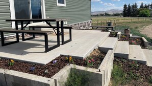 A patio with picnic tables, a stone wall, and flower beds. - Spacious 4-bedroom house in charming rural Powell with media and fitness room (Powell)