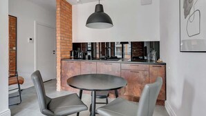 A modern kitchen with a brick accent wall, a round dining table with two chairs, and a pendant light. - Aura III 36 Deluxe | River View | City Center (Gdańsk)