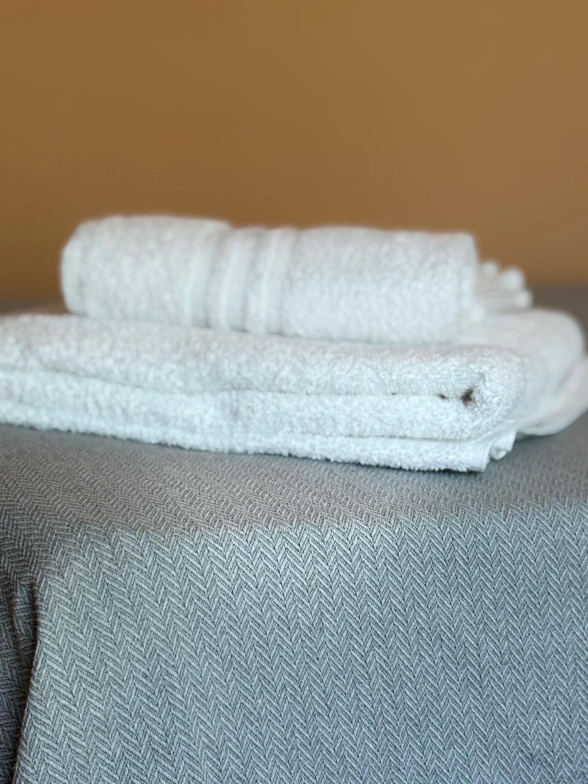 Deux serviettes blanches pliées sont posées l’une sur l’autre sur un coussin gris à texture marquée.