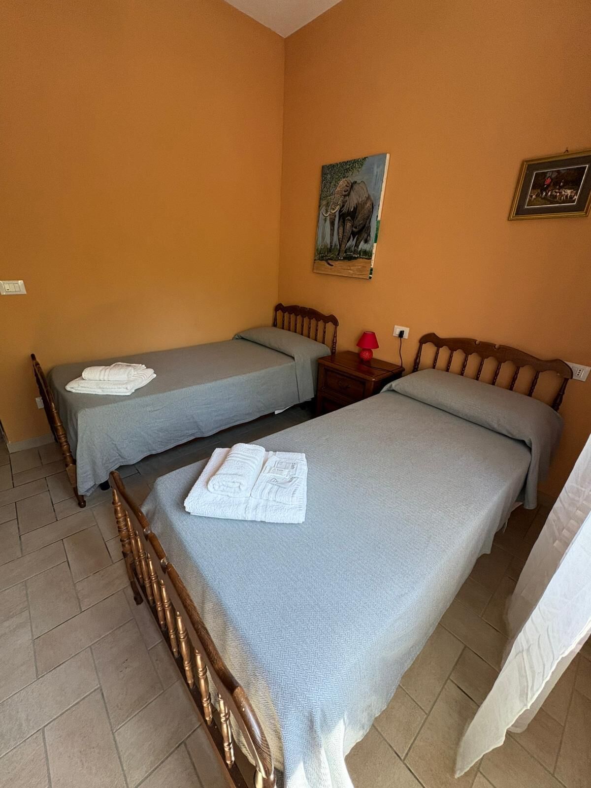 A room with two single beds, a nightstand with a lamp, and a painting on the wall.