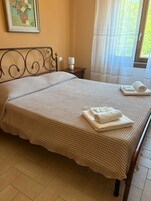 Una cama bien hecha con una colcha a cuadros, una lámpara de noche y una toalla enrollada al lado.