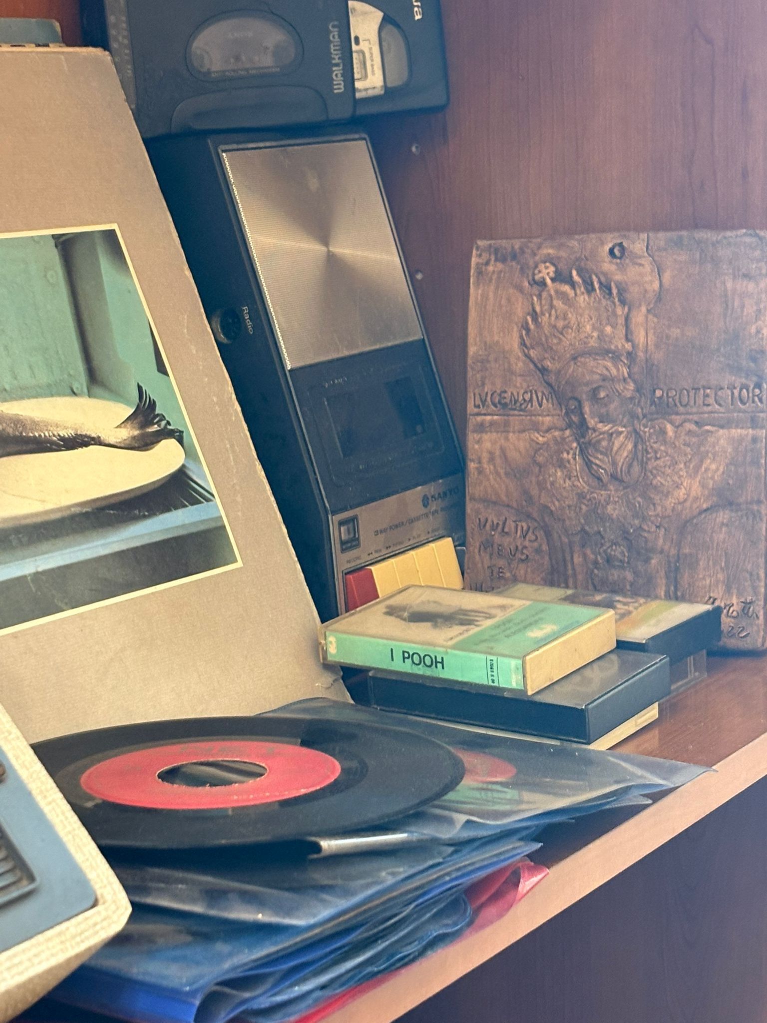 Un escritorio con un reproductor de casetes, un cuadro enmarcado, una pila de libros y una placa decorativa.
