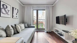 Ein modernes Wohnzimmer mit einem grauen Sofa, einem Flachbildfernseher und Blick auf einen Balkon.