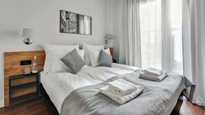 Ein Hotelzimmer mit einem Bett, zwei Nachttischen, einer Wandlampe, einem gerahmten Bild und einem Fenster mit Vorhängen.