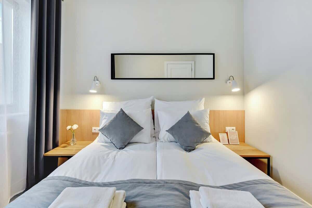 Une chambre d’hôtel avec un grand lit, deux tables de chevet, un miroir et une fenêtre avec des rideaux.