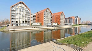 Um prédio de apartamentos moderno com um rio à frente, com varandas e fachadas em tons de vermelho e branco.