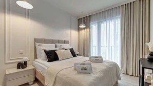 Moderni hotellihuone, jossa on suuri sänky, yöpöydät, yövalaisin ja ikkuna, jossa on verhot.