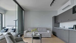 Una sala moderna con un sofá, una mesita de centro y una silla. Hay una zona de cocina con armarios y una encimera.