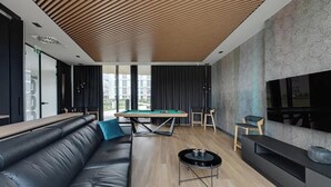 Ein modernes Wohnzimmer mit Billardtisch, Ledersofa und Wand-Fernseher.