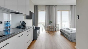 Moderni hotellihuone, jossa on pieni keittiö, ruokailutila, sänky ja suuret ikkunat.