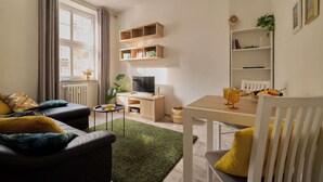 Un salon comprenant un canapé, une table basse, un téléviseur, une bibliothèque et une table à manger avec des chaises.