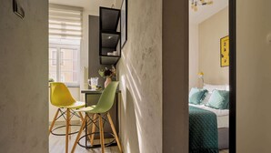 Une pièce comprenant un lit, un bureau avec des chaises, une fenêtre et une étagère fixée au mur.