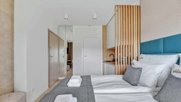 Une chambre d’hôtel avec un lit, une table de chevet, un miroir, une armoire et une salle de bain visible à travers une porte ouverte.