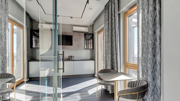 Une cuisine moderne avec une cloison en verre, un coin repas avec deux chaises et une grande fenêtre avec des rideaux.
