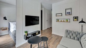 Una sala de estar moderna con un televisor de pantalla plana, un sofá gris, dos taburetes negros y piso de madera.