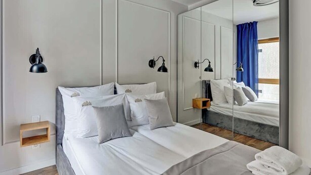 Una habitación de hotel moderna con una cama grande, lámparas de noche, un espejo y vistas al exterior.