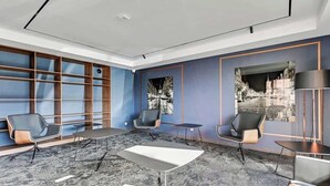 Habitación de hotel moderna con un ventanal grande, un área de descanso con mesa y vistas a un paisaje urbano.