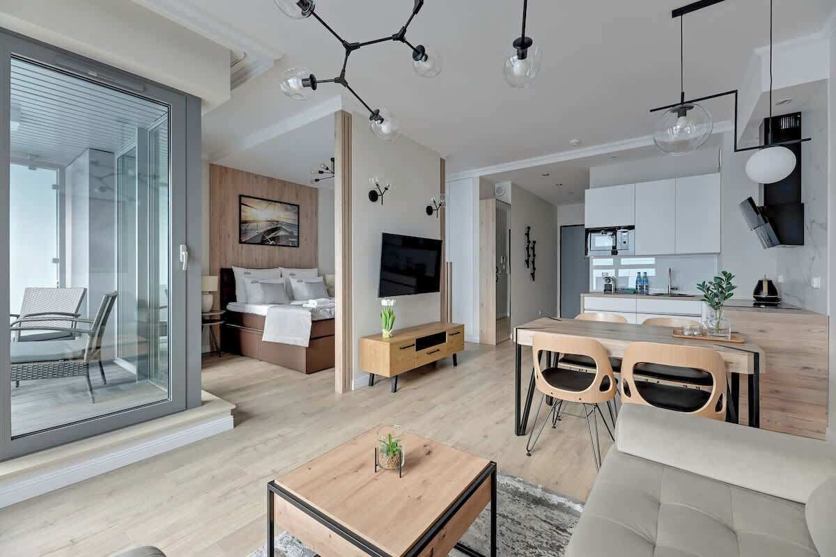 Eine moderne Wohnung mit einer Glastür, einem Holzesstisch, einem Sofa, einem Fernseher, einem Bett und einer Küchenzeile.