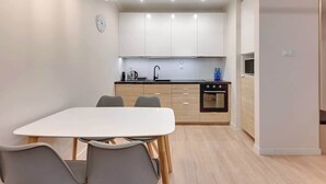 Een moderne keuken met witte kastjes, een zwart fornuis en een eethoek met een witte tafel en grijze stoelen.