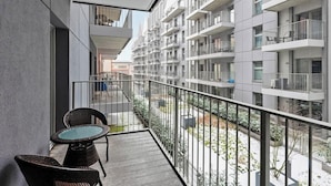Een balkon met rieten stoelen, een klein tafeltje en uitzicht op een woongebouw met balkons.