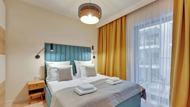 Een hotelkamer met een bed, nachtkastje, lamp, raam met gordijnen en uitzicht.