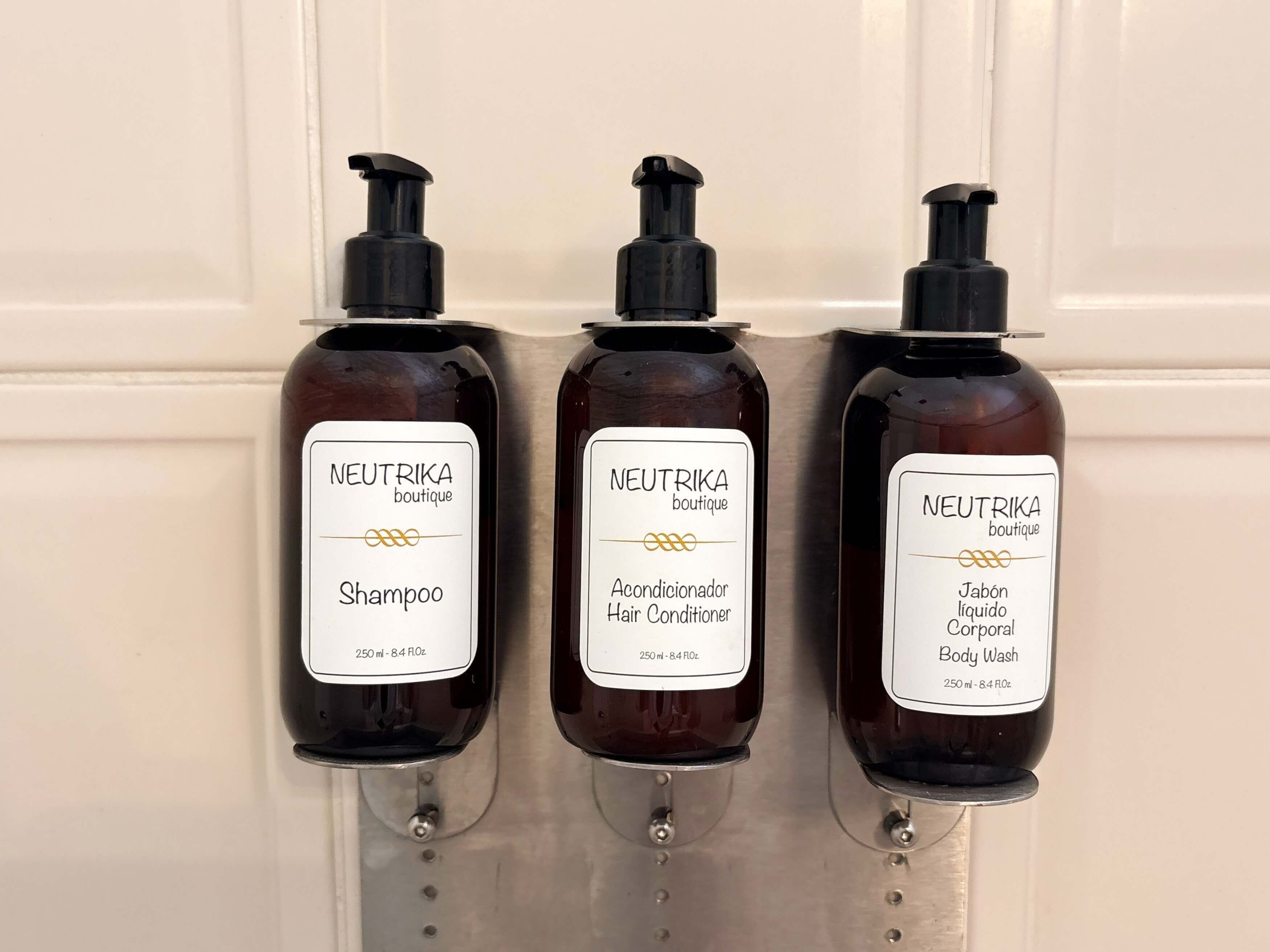 Trois flacons de shampoing, d’après-shampoing et de gel douche de la marque Neutrika, présentés dans un présentoir mural.
