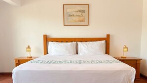 Una cama con cabecera de madera, dos mesitas de noche con lámparas y un cuadro enmarcado en la pared.