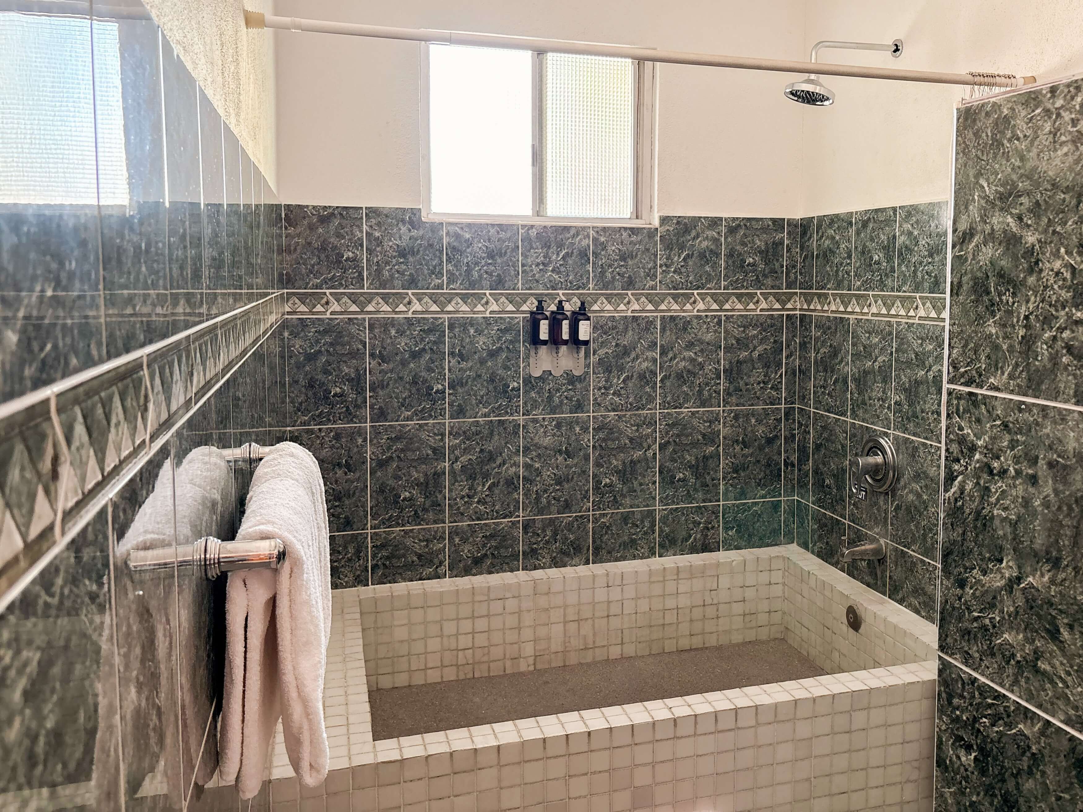 A shower with a glass door, a towel rack with a towel, and a window above the shower.