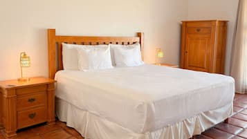 Una cama bien hecha con sábanas blancas, un cabecero de madera, dos lámparas de noche, una mesita de noche con cajones y un armario de madera.