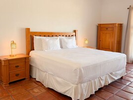 Una cama bien hecha con sábanas blancas, un cabecero de madera, dos lámparas de noche, una mesita de noche con cajones y un armario de madera.